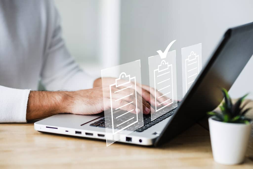 pessoa teclando em um notebook, com imagens de pranchetas. 